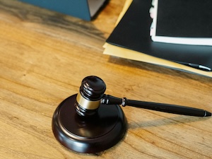 a gavel lying on a wooden surface, likely a desk or table. The gavel is dark, possibly black or a very dark wood, with a gold band around the head.